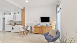 Una cocina moderna con lavadora, un comedor con mesa y sillas, un sofá y una televisión.
