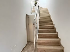Eine Treppe mit Holzboden und Metallgeländer, die zu einer Zwischenebene mit einer Pflanze führt.