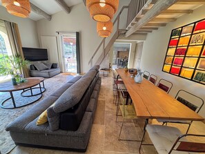 A modern living room with a sofa, dining table, chairs, and a staircase. - THE PROPERTIES: Air-conditioned and with a heated pool, in the Alpilles park (Saint-Rémy-de-Provence)