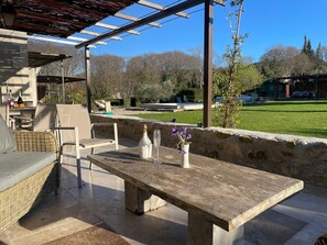 An outdoor patio with a stone table, wicker furniture, and a pergola. - THE PROPERTIES: Air-conditioned and with a heated pool, in the Alpilles park (Saint-Rémy-de-Provence)