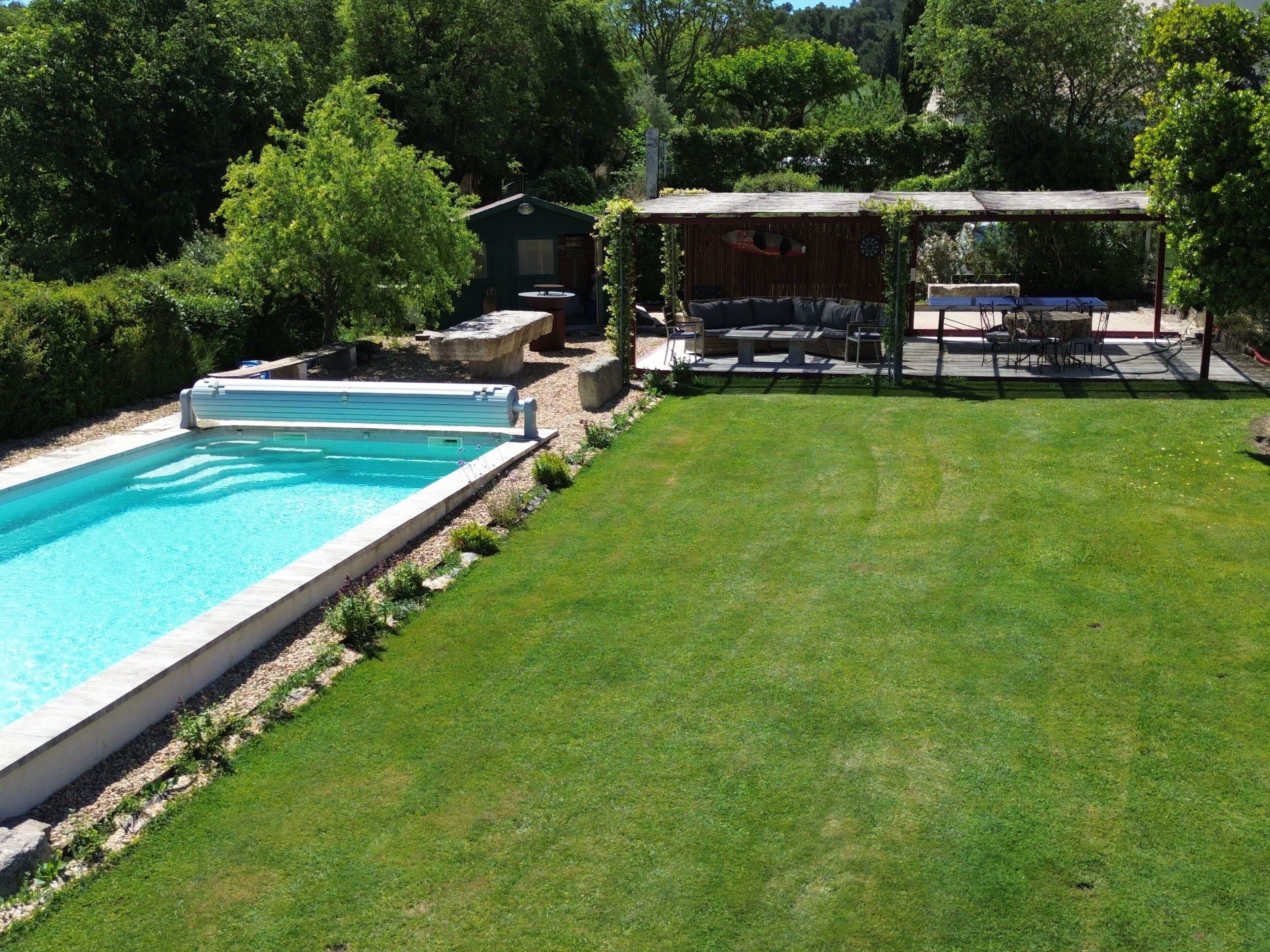 Une piscine avec un espace gazonné et un coin salon abrité.