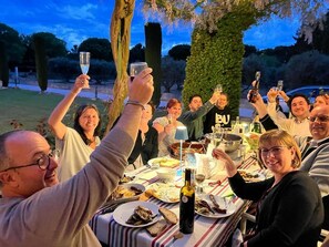 Un groupe de personnes trinquant autour d’une table où sont disposés de la nourriture et des boissons, à l’extérieur, au crépuscule.