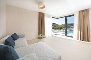 Ein modernes Hotelzimmer mit einer großen Couch, einem kleinen runden Tisch und Blick auf einen Swimmingpool.