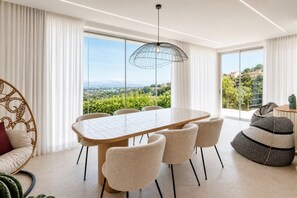 A modern dining area with a large table, chairs, and a view of greenery and buildings. - Villa New Pulicinu – Private pool and panoramic views 🌿💦 (Arzachena)