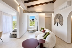 Ein modernes Wohnzimmer mit einer gebogenen Couch, einem runden Tisch und einem großen Fenster mit Blick auf Grünflächen.