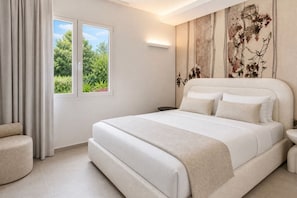 Ein Schlafzimmer mit einem großen Bett, einem Nachttisch, einem Sessel und einem Fenster mit Vorhängen.
