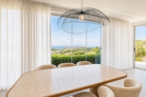 Ein Essbereich mit Tisch und Stühlen, einer modernen Pendelleuchte und Blick auf Grünflächen sowie eine entfernte Landschaft durch große Fenster.
