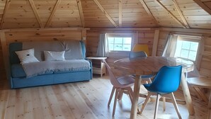 Ein gemütliches Dachzimmer mit Holzbalkendecke, einem blauen Sofa, einem Esstisch mit Stühlen und einem Fenster, das natürliches Licht hereinlässt.
