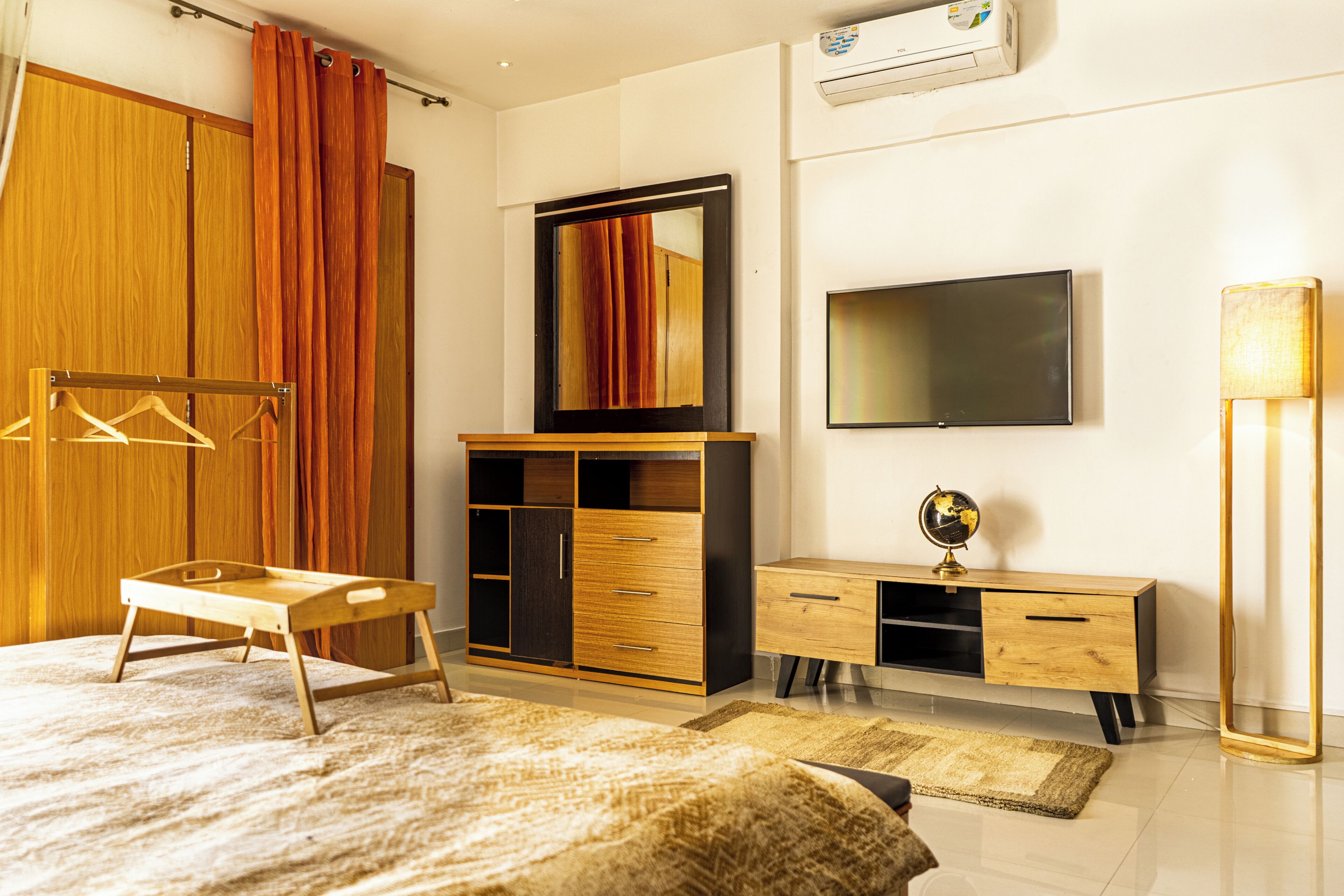 Un dormitorio con cama, armario de madera, escritorio con cajones, televisor de pantalla plana, un globo terráqueo y una lámpara de pie.