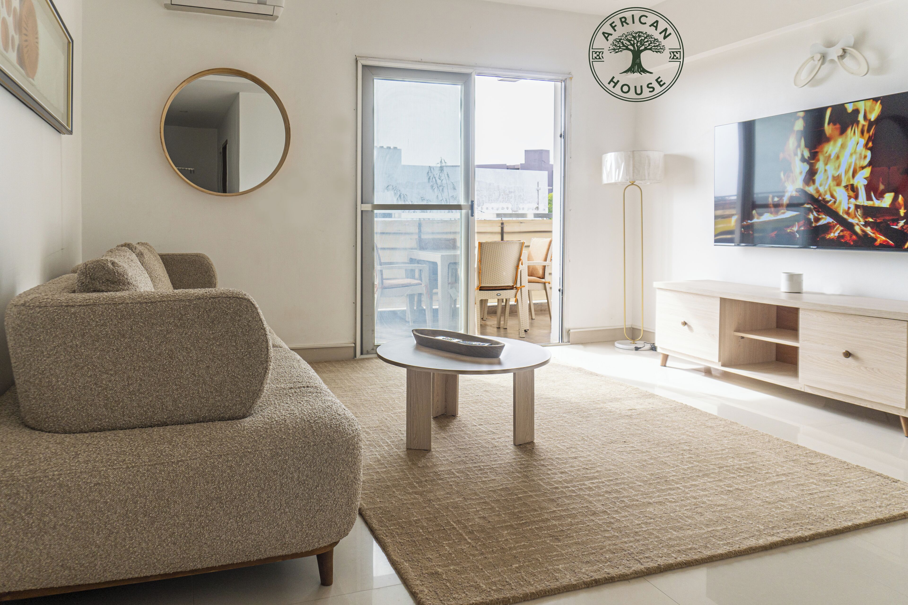 A living room with a sofa, a coffee table, a TV, a mirror, and a sliding glass door leading to an outdoor area.