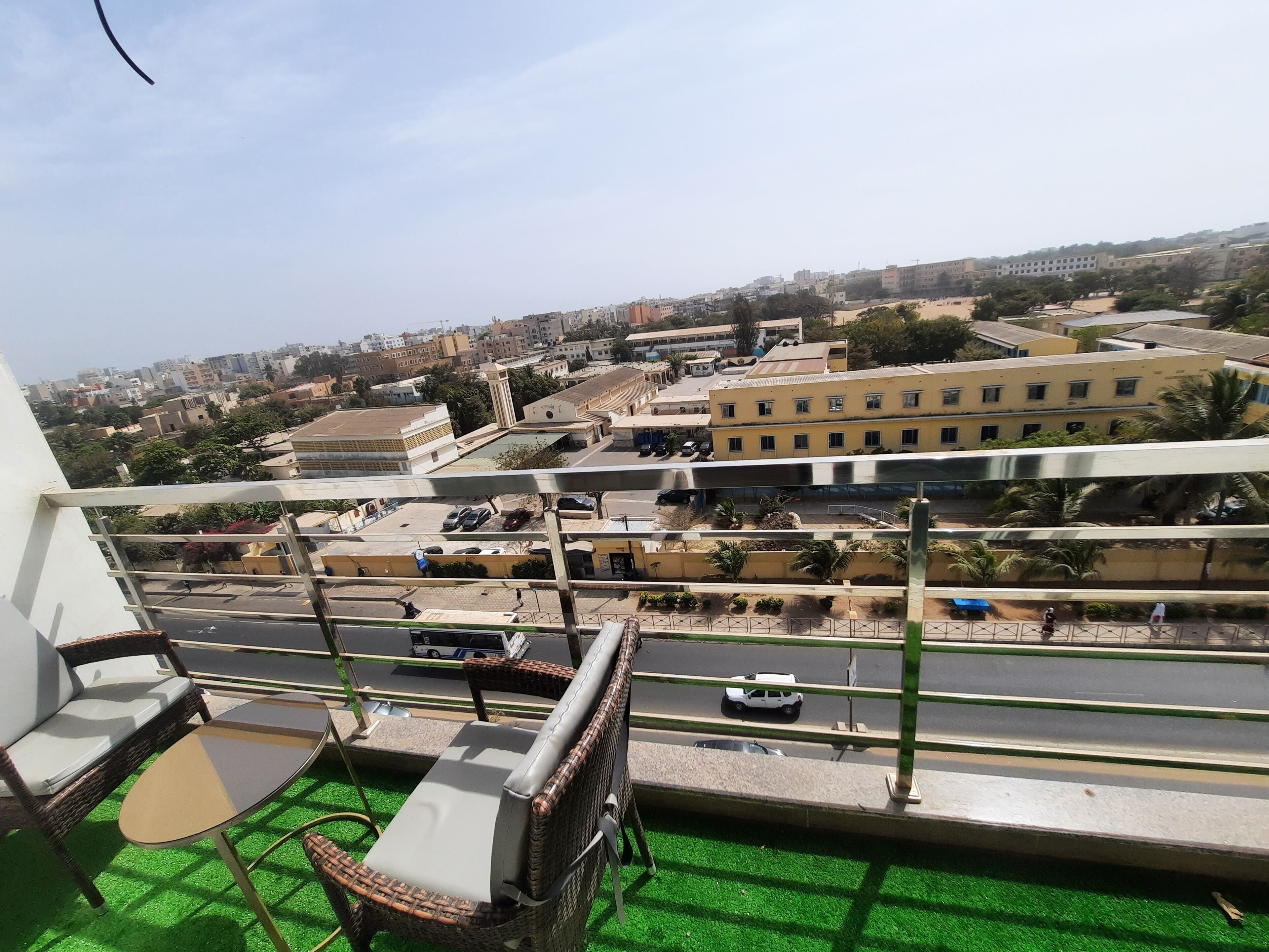 A balcony with wicker furniture, a view of a cityscape, and a road with vehicles.
