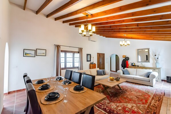 Un comedor con una mesa de madera dispuesta para cuatro personas, un sofá y una alfombra estampada.