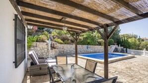 Une terrasse extérieure avec une table et des chaises en verre, un mur en pierre et une piscine.