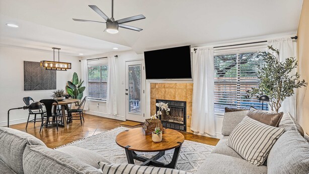 A living room with a sofa, a coffee table, a fireplace, a TV, and a dining area with chairs and a table. - Stylish Backyard Retreat BBQ Workspace (Austin)