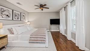 A bedroom with a bed, a ceiling fan, a TV, and artwork on the wall. - Stylish Backyard Retreat BBQ Workspace (Austin)