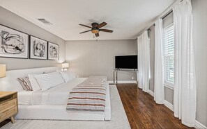 A bedroom with a bed, a ceiling fan, a TV, and artwork on the wall. - Stylish Backyard Retreat BBQ Workspace (Austin)