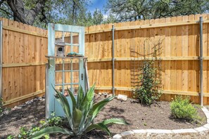 A wooden fence, a birdhouse, and a small garden with plants. - Stylish Backyard Retreat BBQ Workspace (Austin)