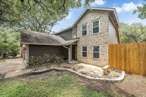 A two-story house with a stone facade, a garage, and a wooden fence. - Stylish Backyard Retreat BBQ Workspace (Austin)