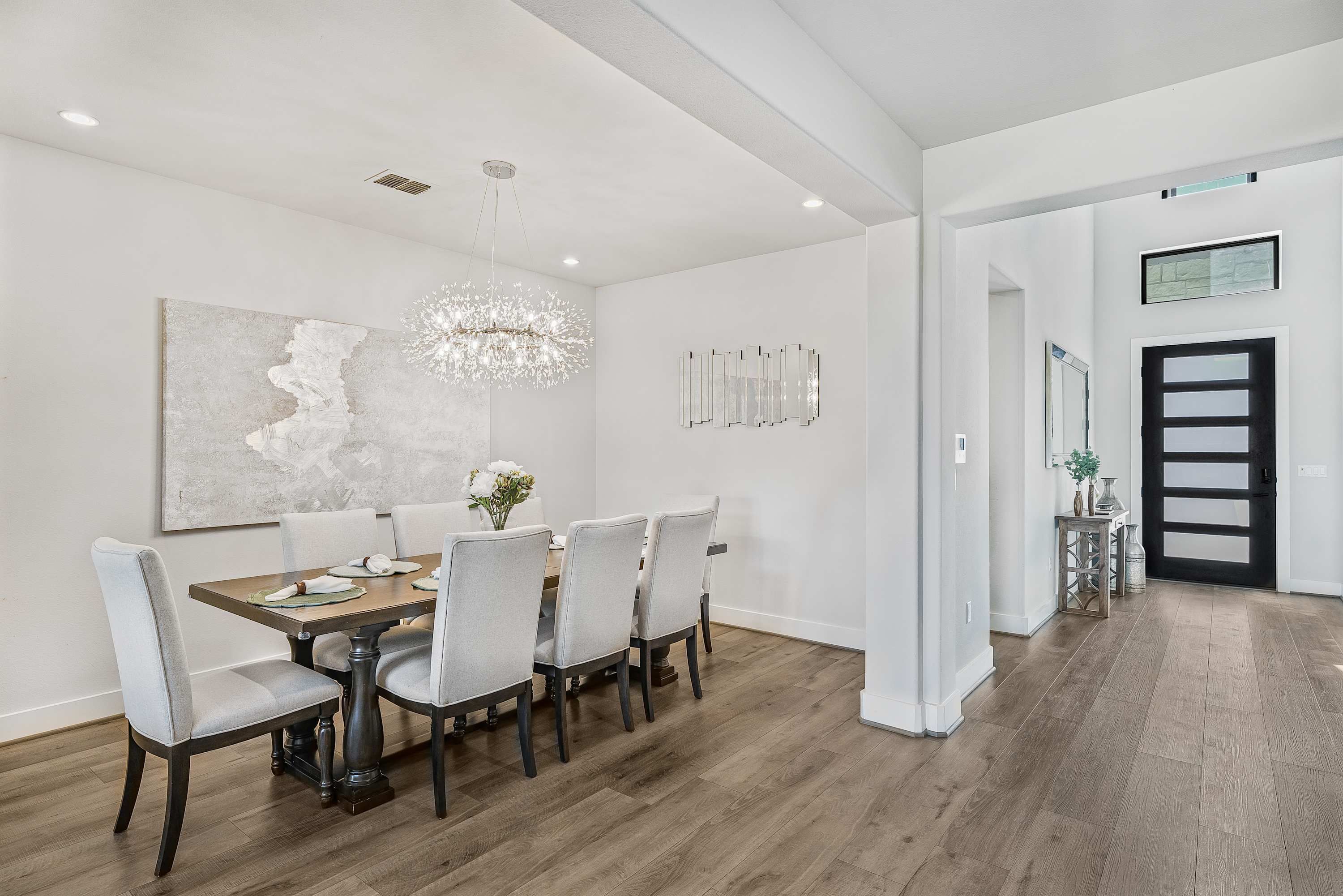A dining room with a wooden table, six chairs, a chandelier, and a large abstract painting on the wall.