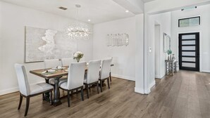 Une salle à manger avec une table en bois, six chaises, un lustre et un grand tableau abstrait accroché au mur.