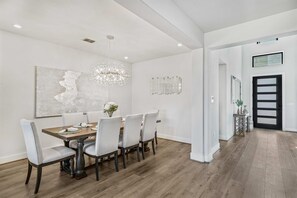 A dining room with a wooden table, six chairs, a chandelier, and a large abstract painting on the wall. - Modern Home w Outdoor Entertaining Space (Austin)