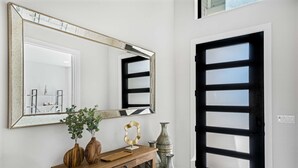 Un couloir avec un grand miroir, une console en bois ornée d’objets décoratifs et une porte à cadre noir.