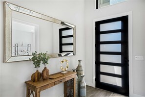 A hallway with a large mirror, a wooden console table with decorative items, and a black-framed door. - Modern Home w Outdoor Entertaining Space (Austin)