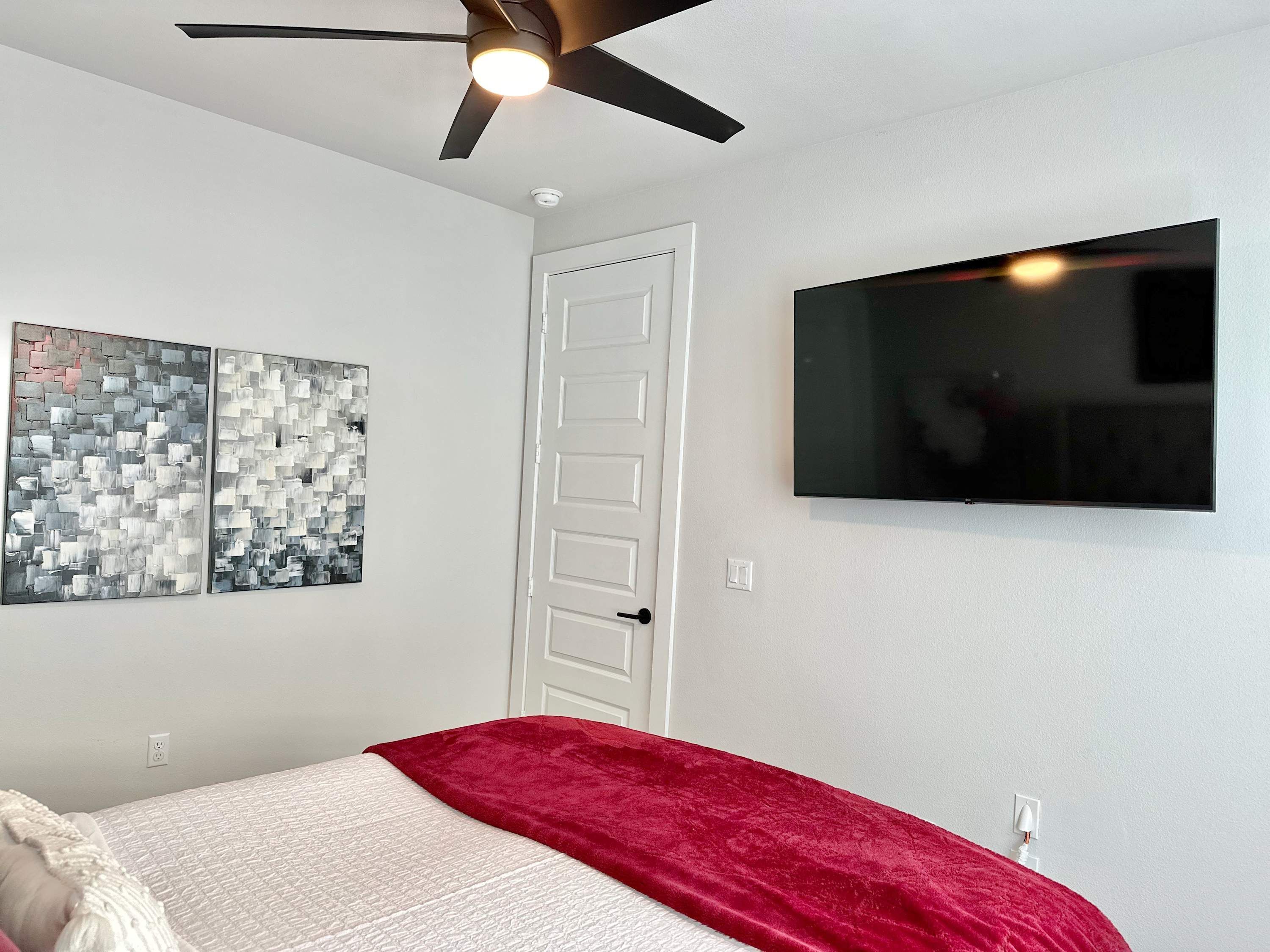 A bedroom with a bed, a ceiling fan, a TV, and two abstract wall art pieces.