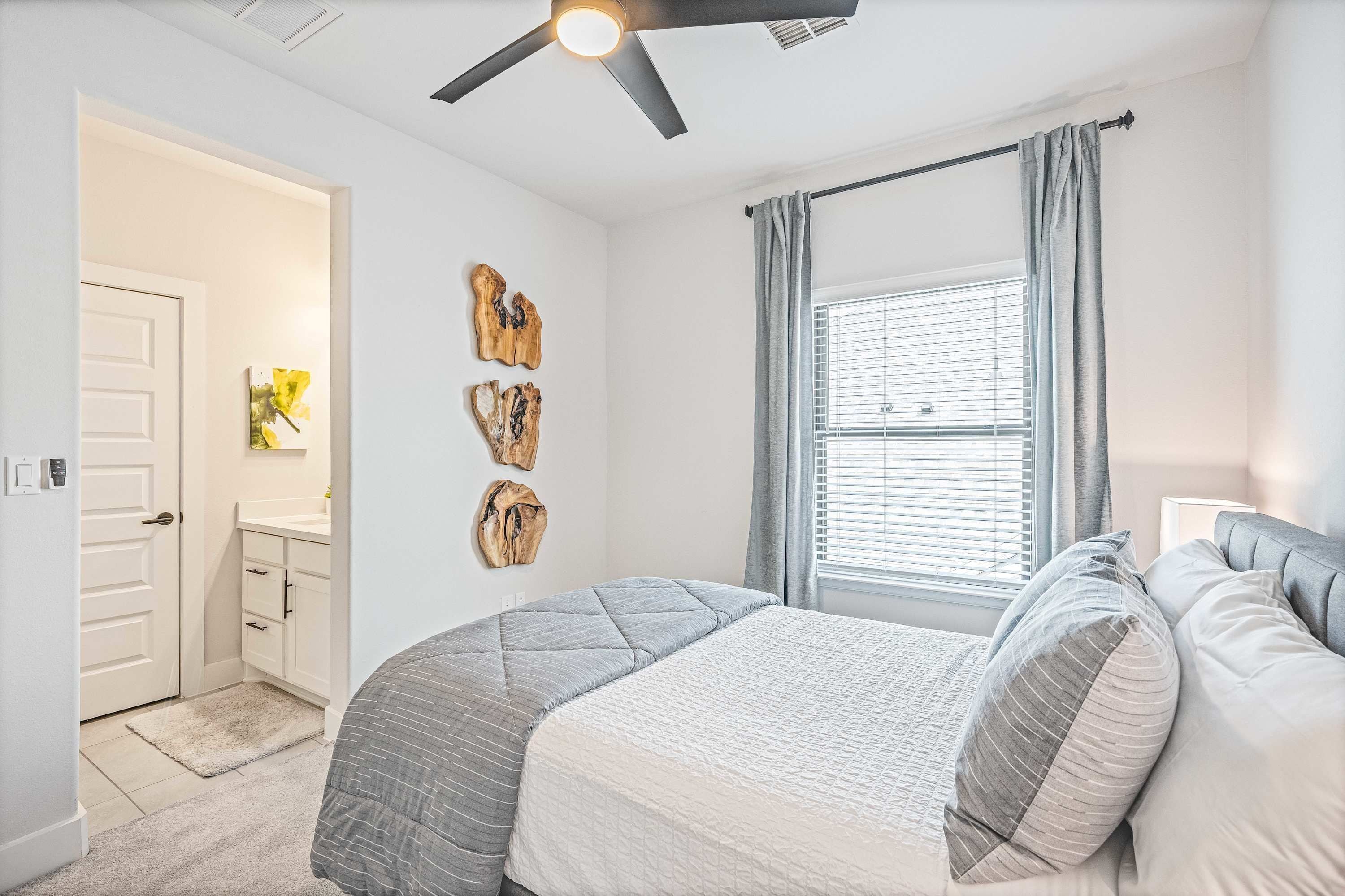 Ein Schlafzimmer mit Bett, Deckenventilator, Fenster mit Vorhängen und Wandbildern.