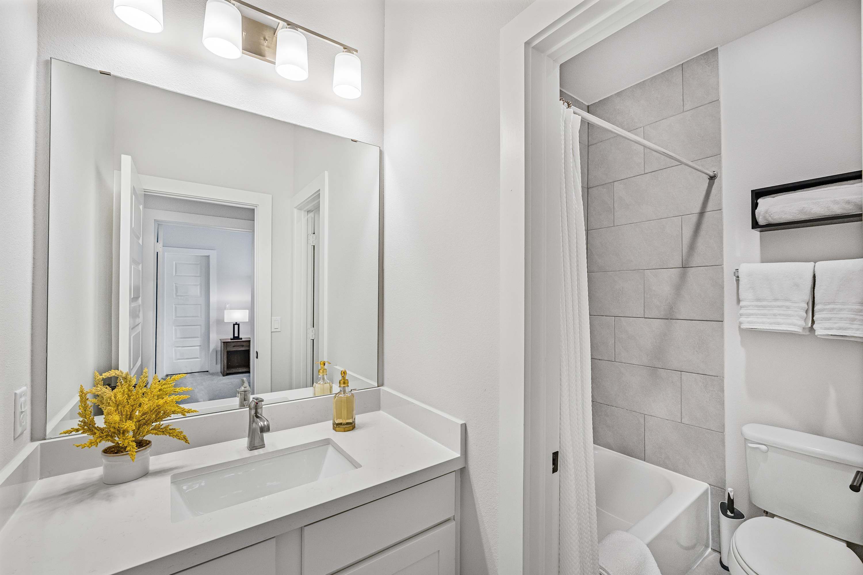 Un baño moderno con lavamanos, espejo y ducha blancos.