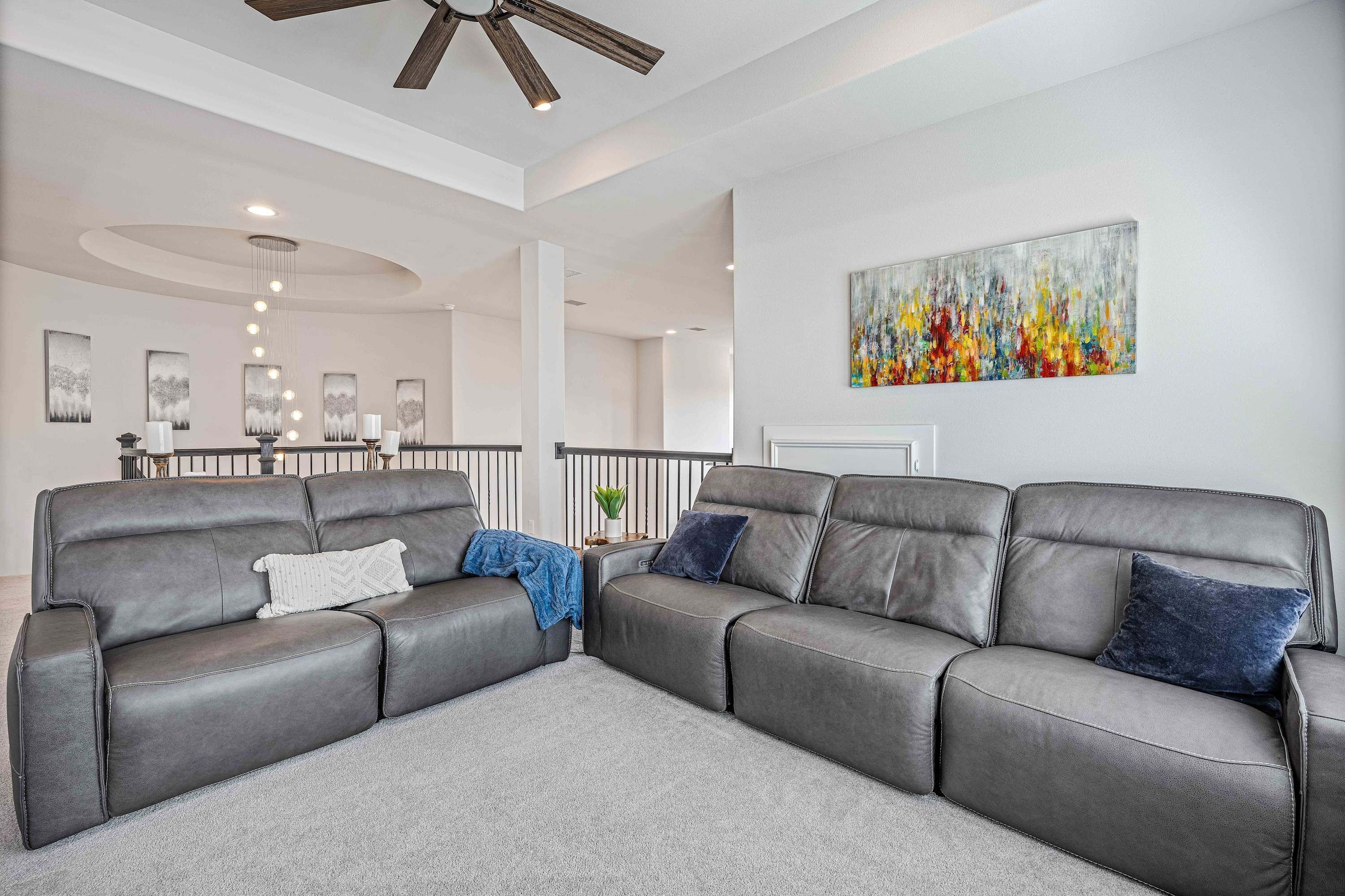 A modern living room with a sectional sofa, a ceiling fan, and a large abstract painting on the wall.