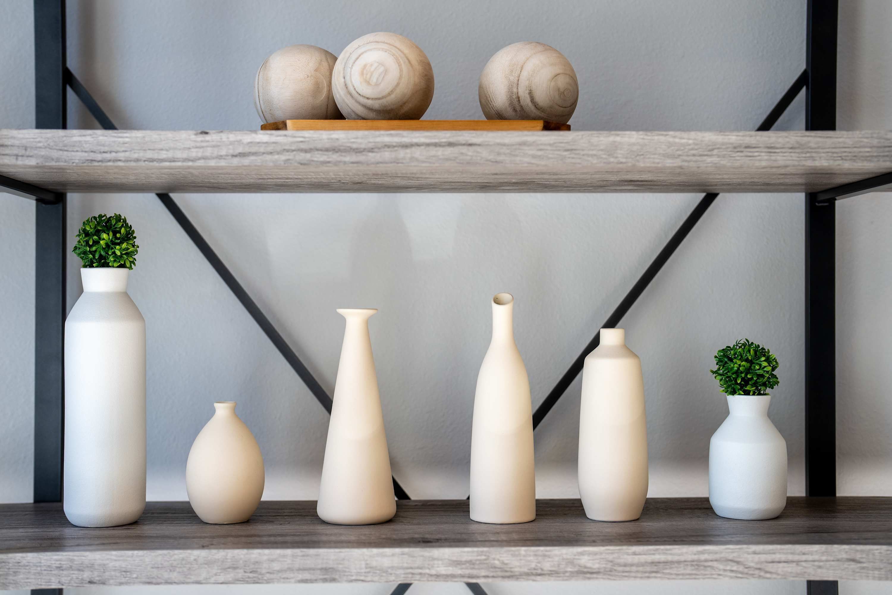 A shelf with six white vases of varying shapes and sizes, a small potted plant, and three wooden decorative balls.
