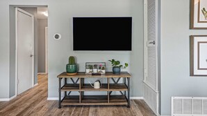 Een hal met een houten console tafel, een wandtelevisie en een deur naar een andere kamer.