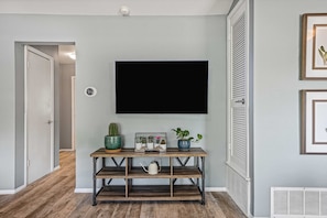 Ein Flur mit einem hölzernen Konsolentisch, einem an der Wand befestigten Fernseher und einer Tür zu einem weiteren Raum.