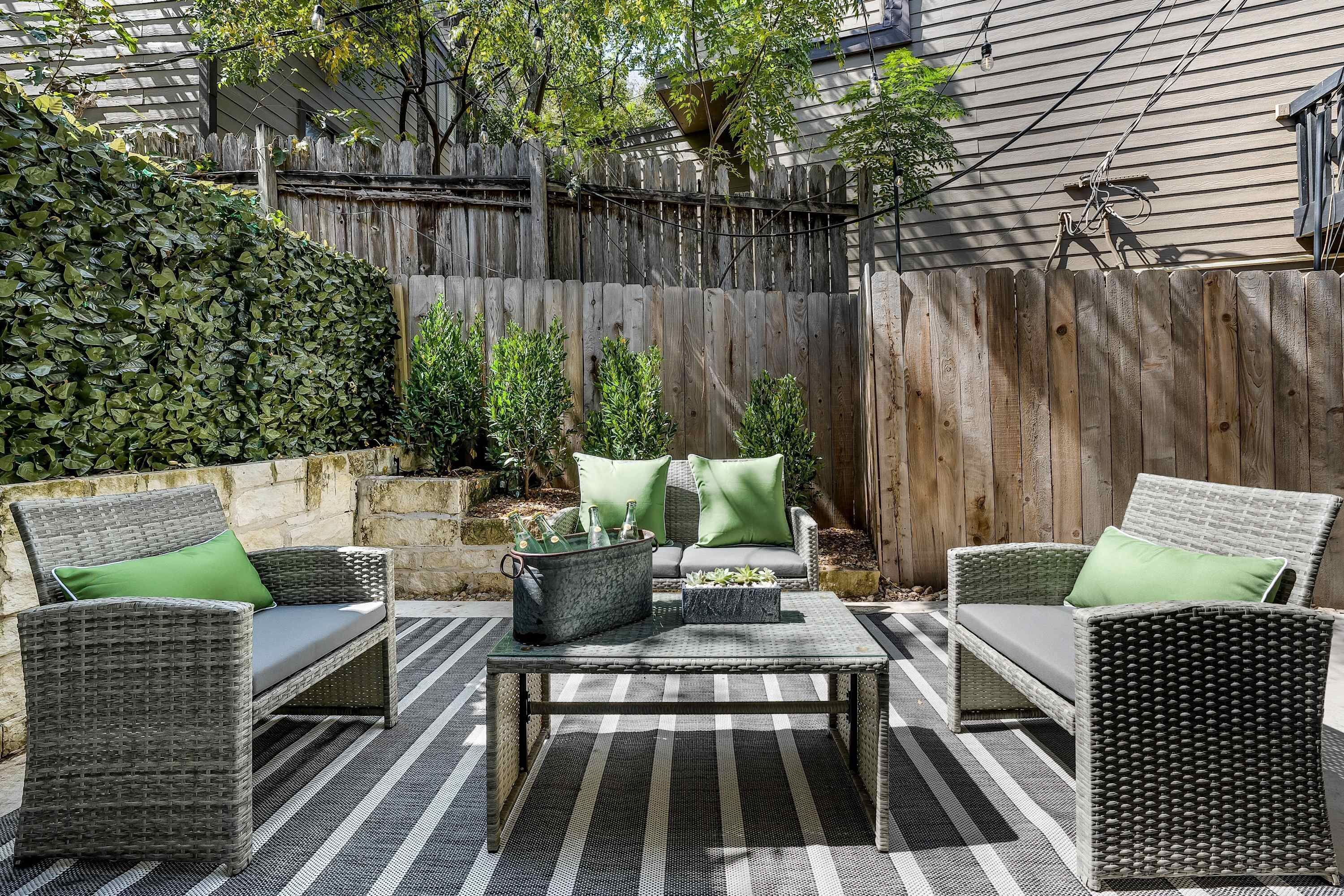 A patio with wicker furniture, a striped rug, and a wooden fence.