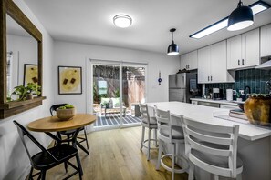 A modern kitchen with white cabinets, a large island, and a dining area with a round table and chairs. - Peaceful Sola Hideaway w Private Patio (Austin)