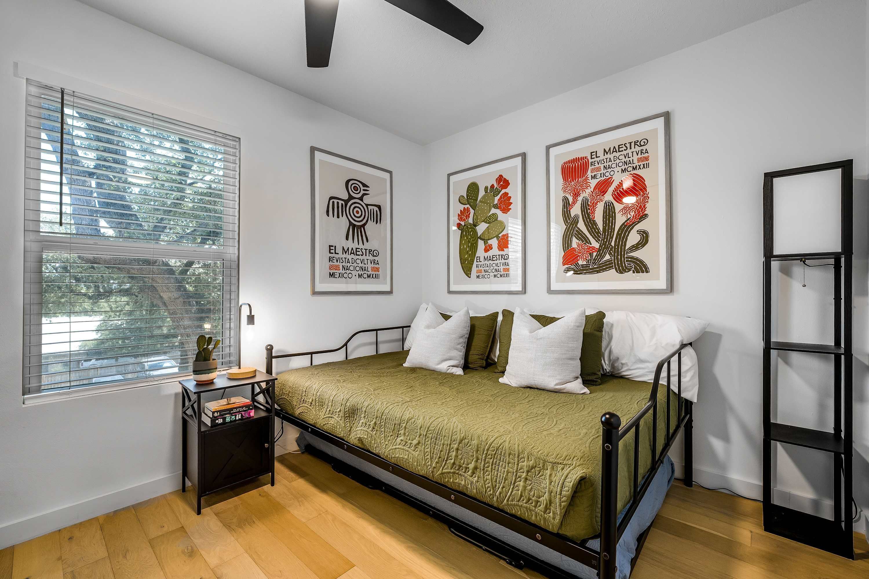 Um quarto com cama, mesa de cabeceira, janela com persianas e três quadros na parede.