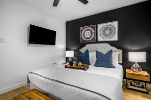 Ein modernes Schlafzimmer mit einem großen Bett, Nachttischen mit Lampen, einem Flachbildfernseher und zwei Wandbildern.