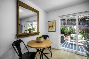 A dining area with a round table, chairs, a bowl of fruit, a mirror, and a sliding glass door leading to an outdoor patio. - Peaceful Sola Hideaway w Private Patio (Austin)