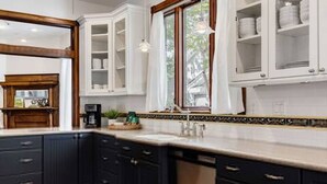 A kitchen with dark cabinetry, white upper cabinets, a window with curtains, and a tiled backsplash. - Charming 5 Bedroom Home in Austin (Austin)