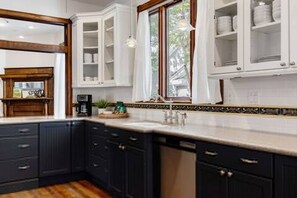 A kitchen with dark cabinetry, white upper cabinets, a window with curtains, and a tiled backsplash. - Charming 5 Bedroom Home in Austin (Austin)