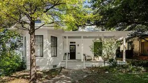 A white house with a front porch, a tree in the foreground, and a clear sky. - Charming 5 Bedroom Home in Austin (Austin)
