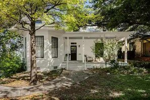 A white house with a front porch, a tree in the foreground, and a clear sky. - Charming 5 Bedroom Home in Austin (Austin)