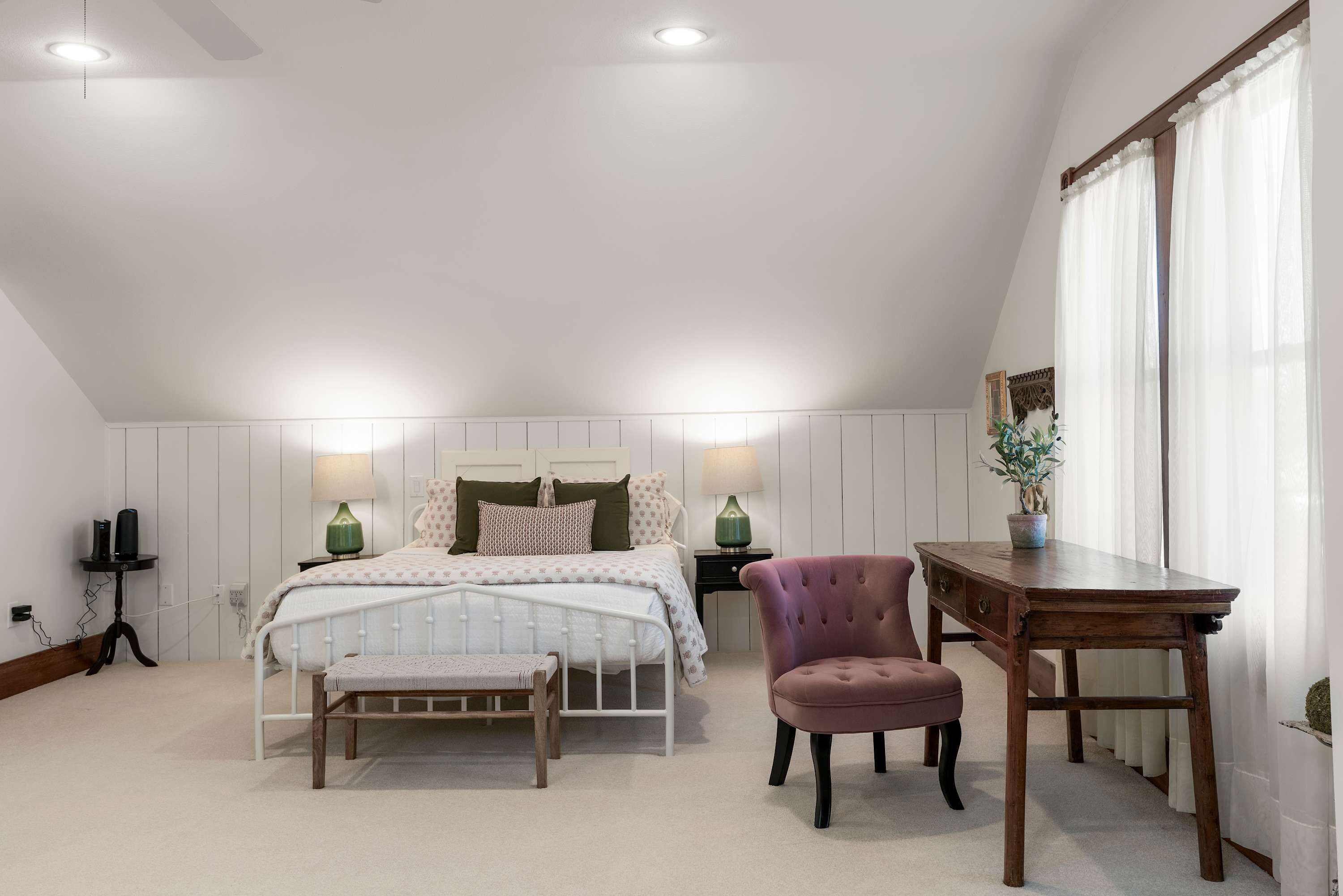 Une chambre à coucher avec un lit, des tables de chevet, une chaise, un bureau et une fenêtre avec des rideaux.