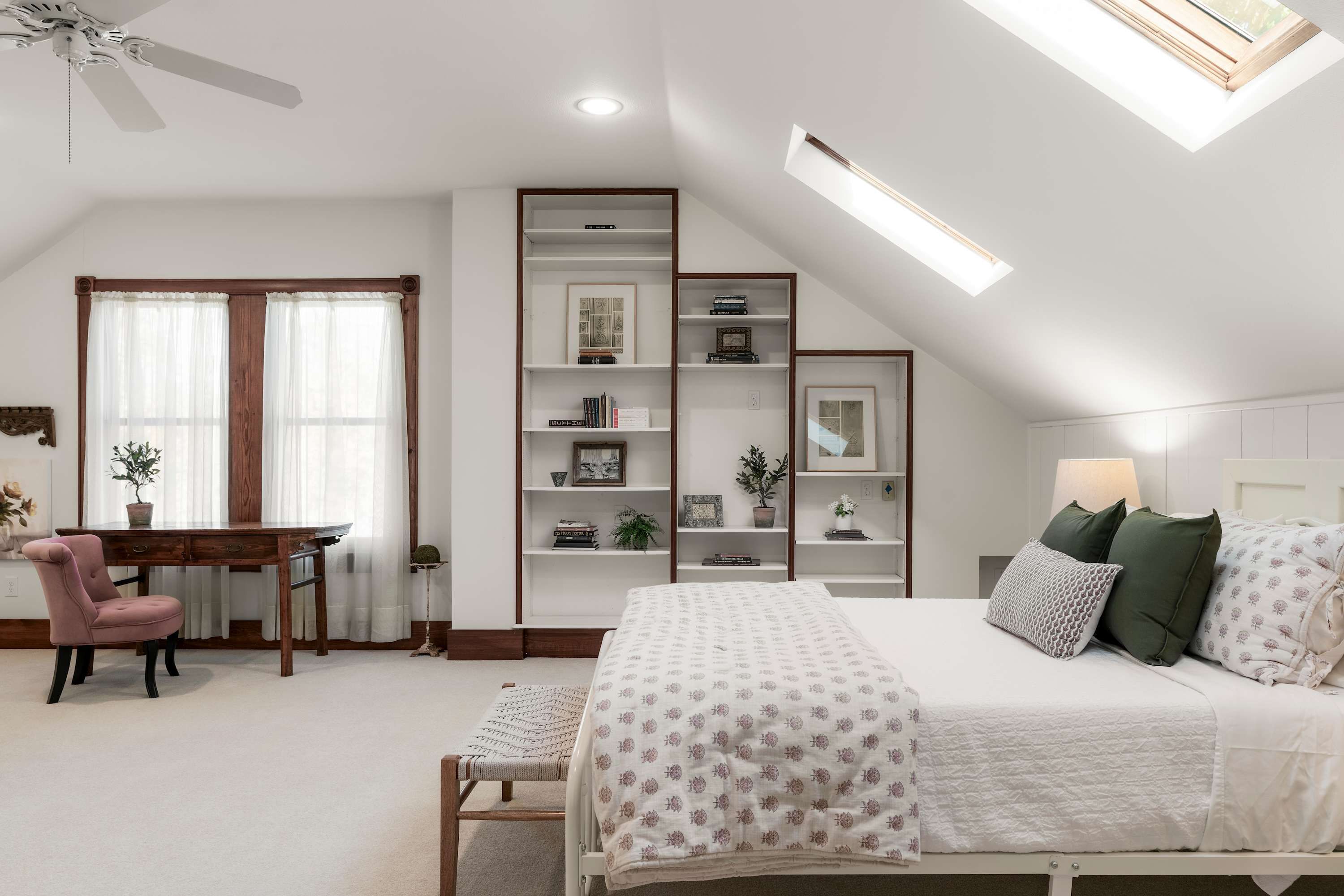 A bedroom with a bed, a desk, a chair, a bookshelf, and a skylight.