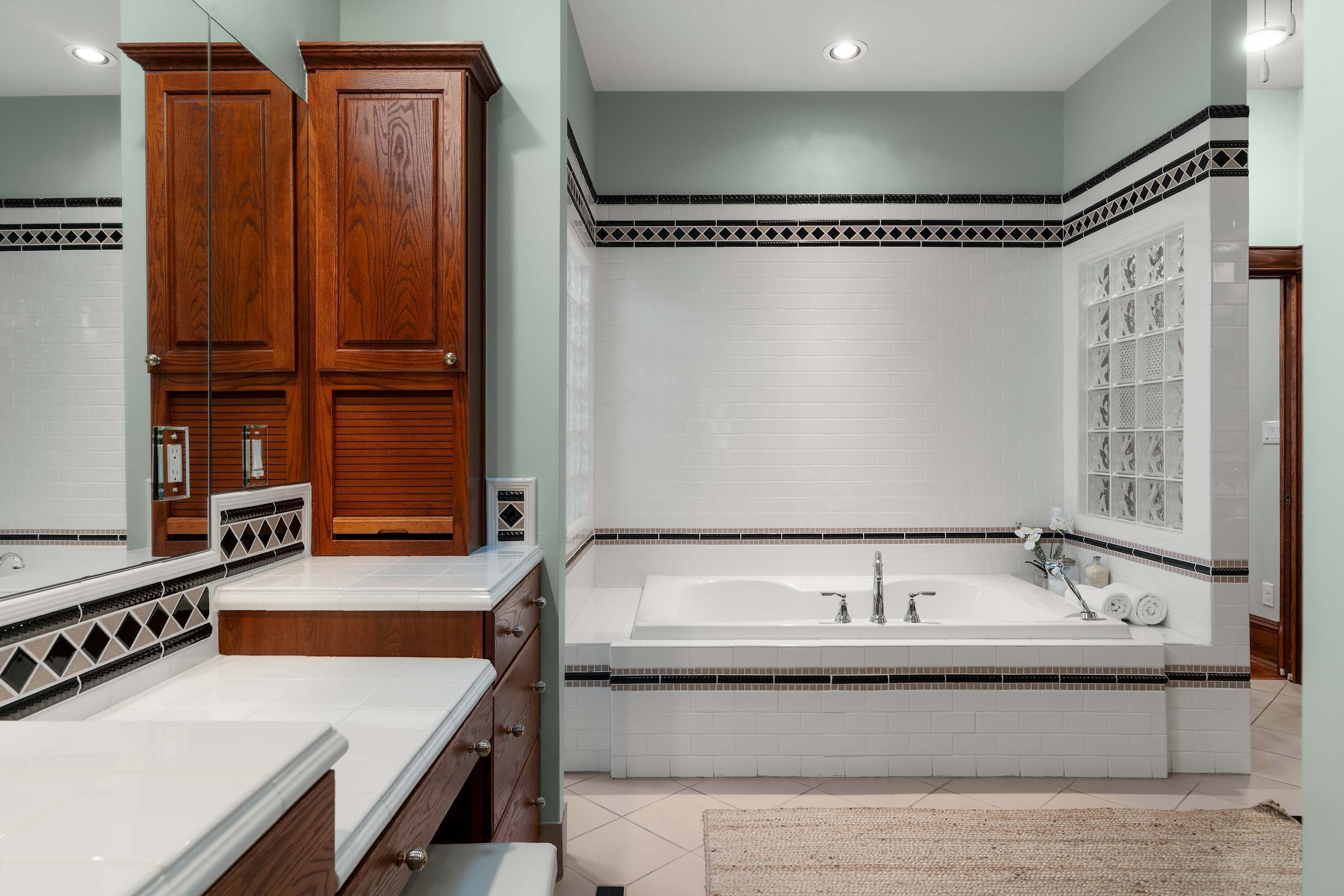 Un baño con una bañera grande, armarios de madera y salpicadero de azulejos.