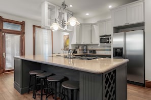 A kitchen with a central island, bar stools, stainless steel appliances, and a pendant light fixture. - Charming 5 Bedroom Home in Austin (Austin)