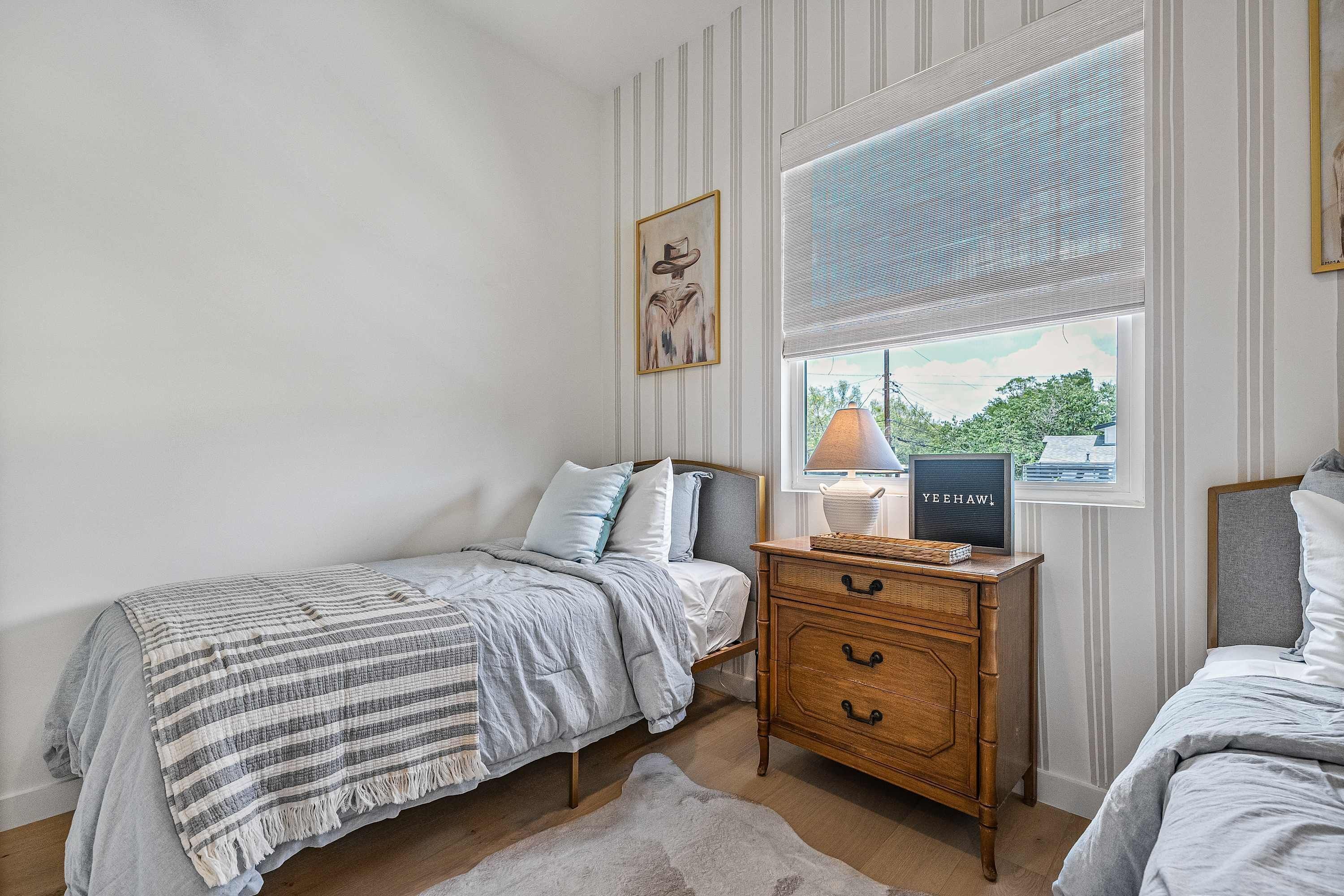 A bedroom with two beds, a dresser, a window with a view, and a framed picture on the wall.