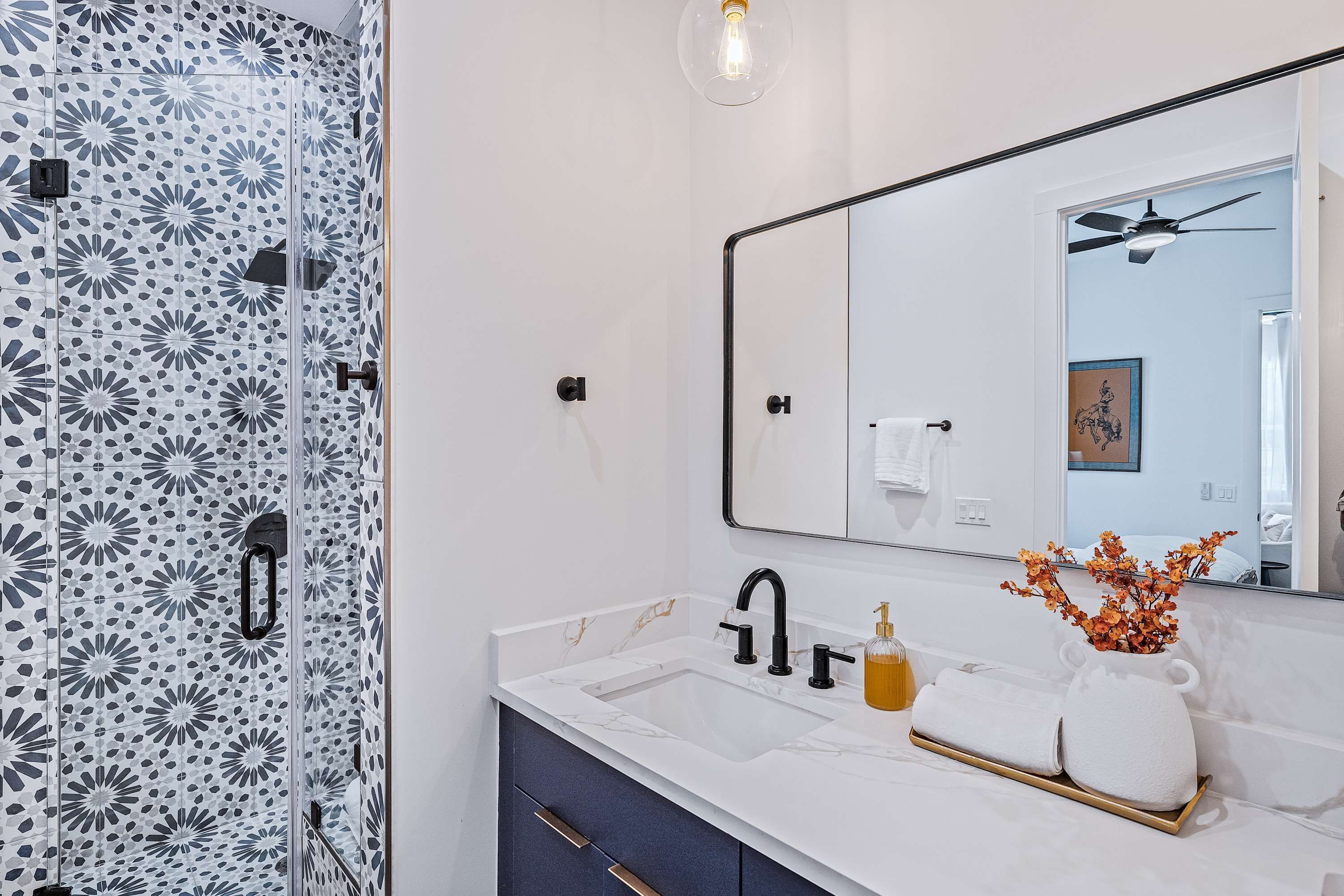 Un baño con ducha, lavamanos con espejo y perchero para toallas.