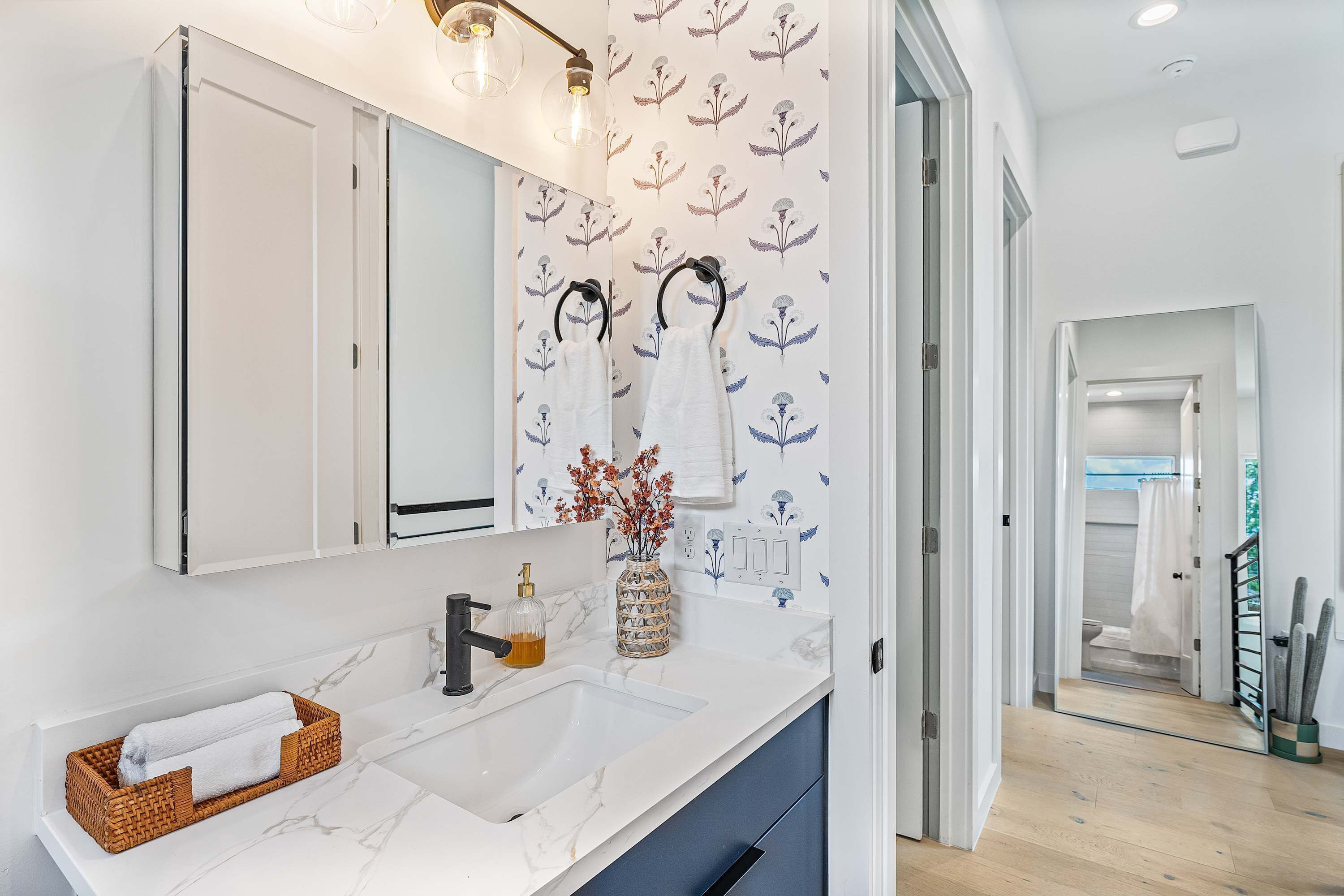 Un bagno moderno con un lavandino bianco, uno specchio e un vaso con fiori secchi.